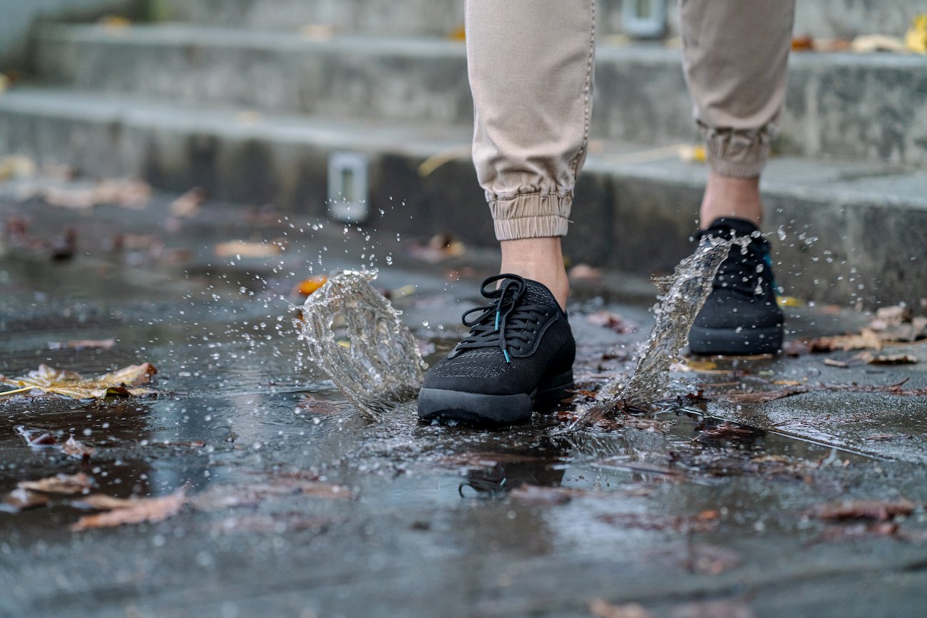 Man wearing black shoes stepping on a muddy puddle 